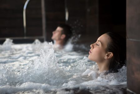 Side view of wet-haired adult woman with eyes closed in bubbled water in spa