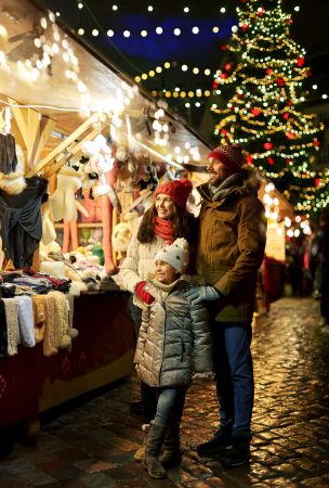 family, winter holidays and celebration concept - happy mother, father and little daughter at christmas market on town hall square in tallinn, estonia