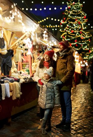 happy family at christmas market in city family, winter holidays and celebration concept - happy mother, father and little daughter at christmas market on town hall square in tallinn, estonia