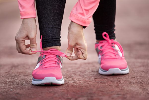 Runner woman tying up laces of shoes, getting ready to run for cardio and weight loss, no face