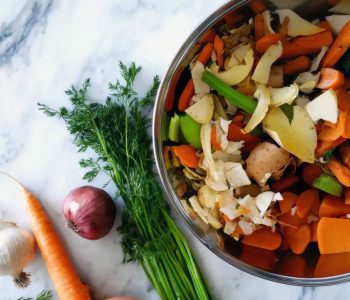 Top view of a metal bowl filled with vegetable scraps—peels, husks, and stems—on a white marble counter. Rustic and eco-conscious mood-min Top view of a metal bowl filled with vegetable scraps—peels, husks, and stems—on a white marble counter. Rustic and eco-conscious mood-min